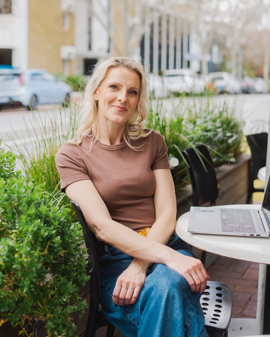Tash Miller smiling at an outdoor café table with her laptop