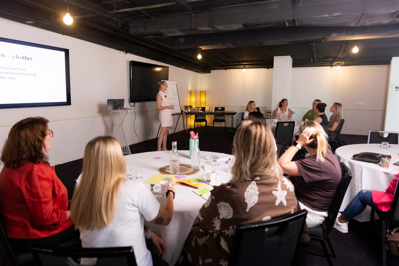 Tash Miller presenting to a full workshop room of business owners at round tables